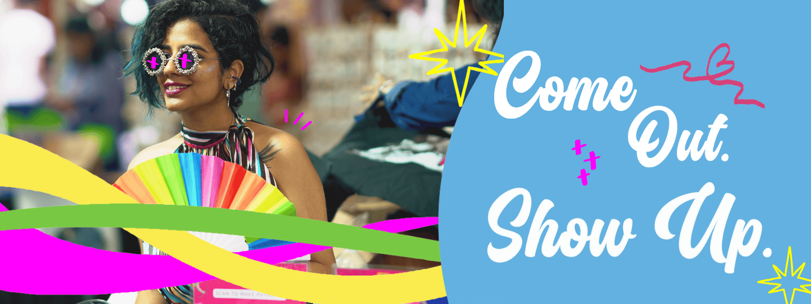 Person holding a rainbow fan at Maya Bazaar, with the words “Come Out. Show up” in bold festive design.